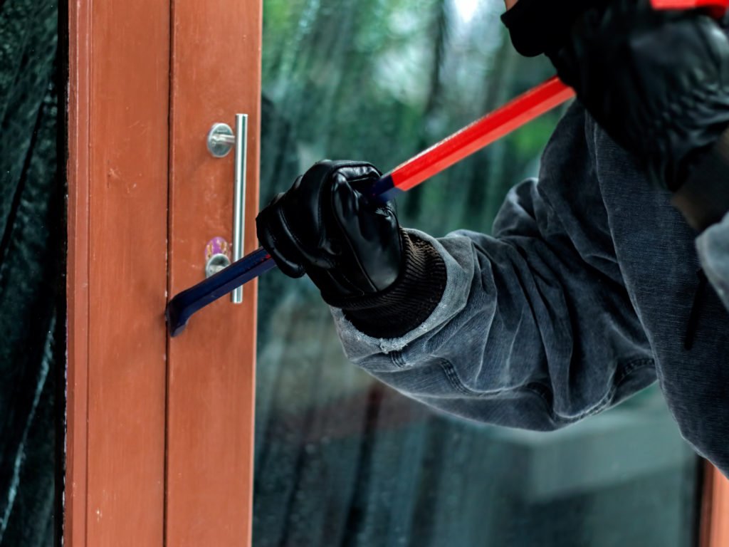 Burglar with crowbar trying break the door to enter the house